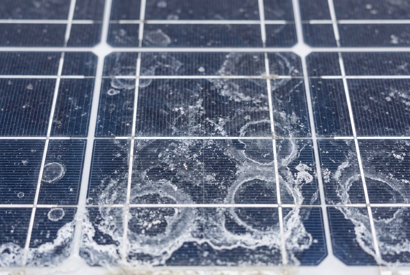 Dried white hard-water mineral spots and limescale rings on the glass of a solar panel